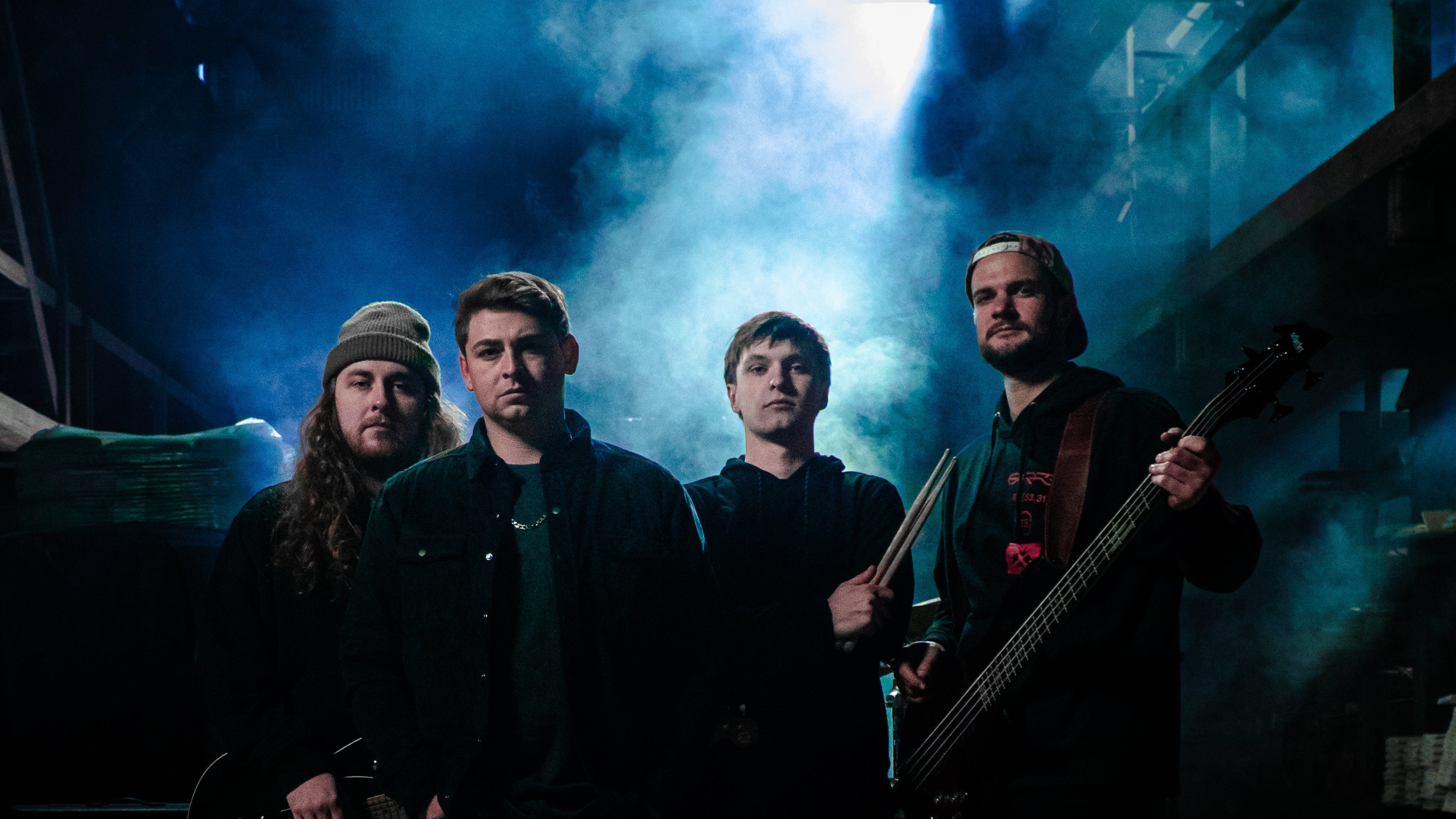 Four band members posing with their instruments in a dark, smoky setting